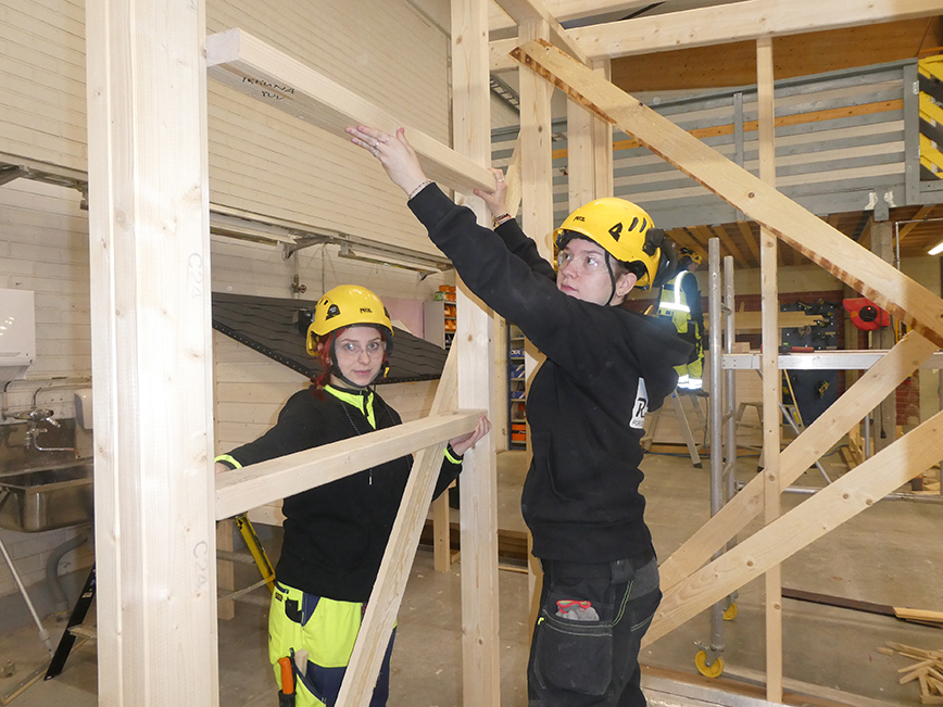 Kaksi rakennusalan opiskelijaa rakentamassa kehikkoa sisätiloissa.
