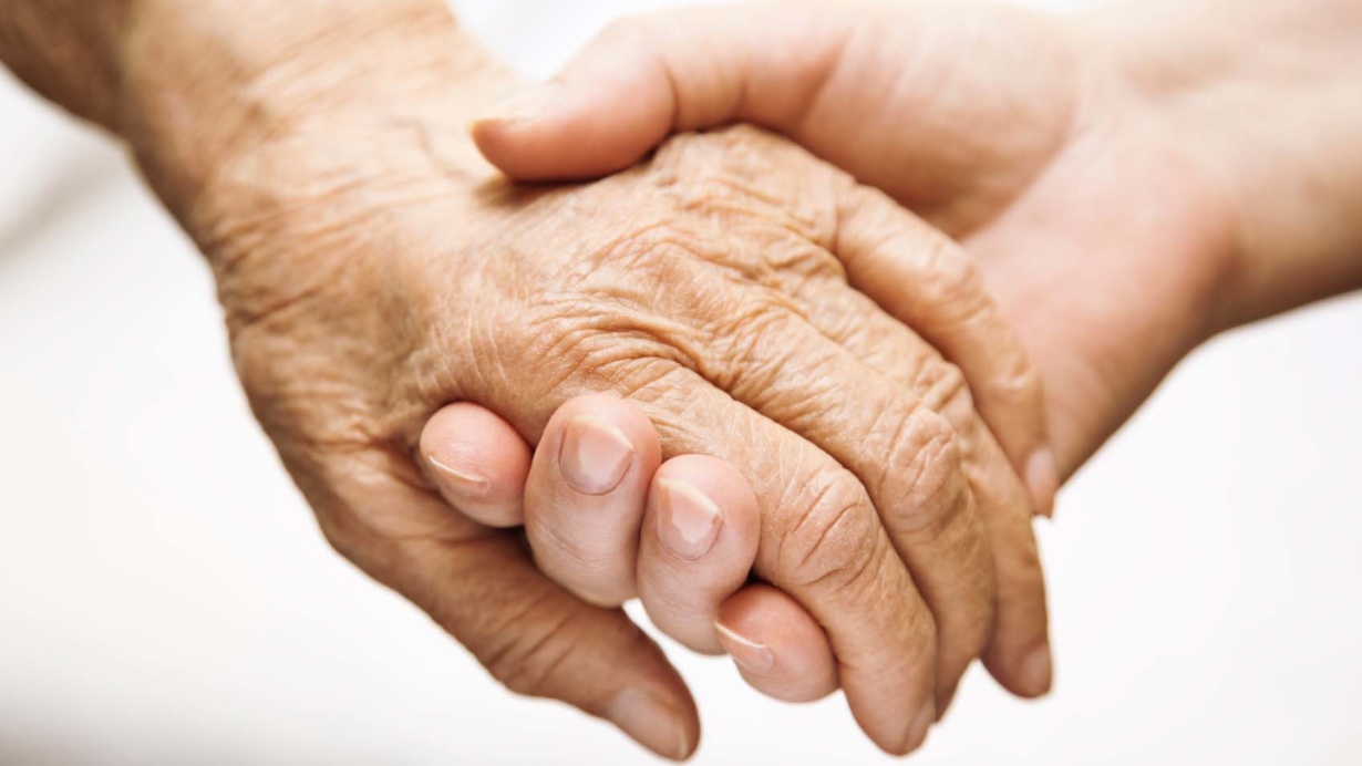 Hoitaja pitää vanhusta kädestä kiinni