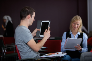 Mies iPadin kanssa ja nainen kannettavan tietokoneen äärellä tekemässä yhteistyötä.