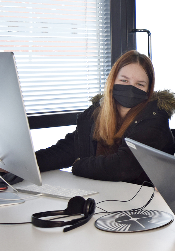 Nainen istuu tietokoneen äärellä maski päällä.