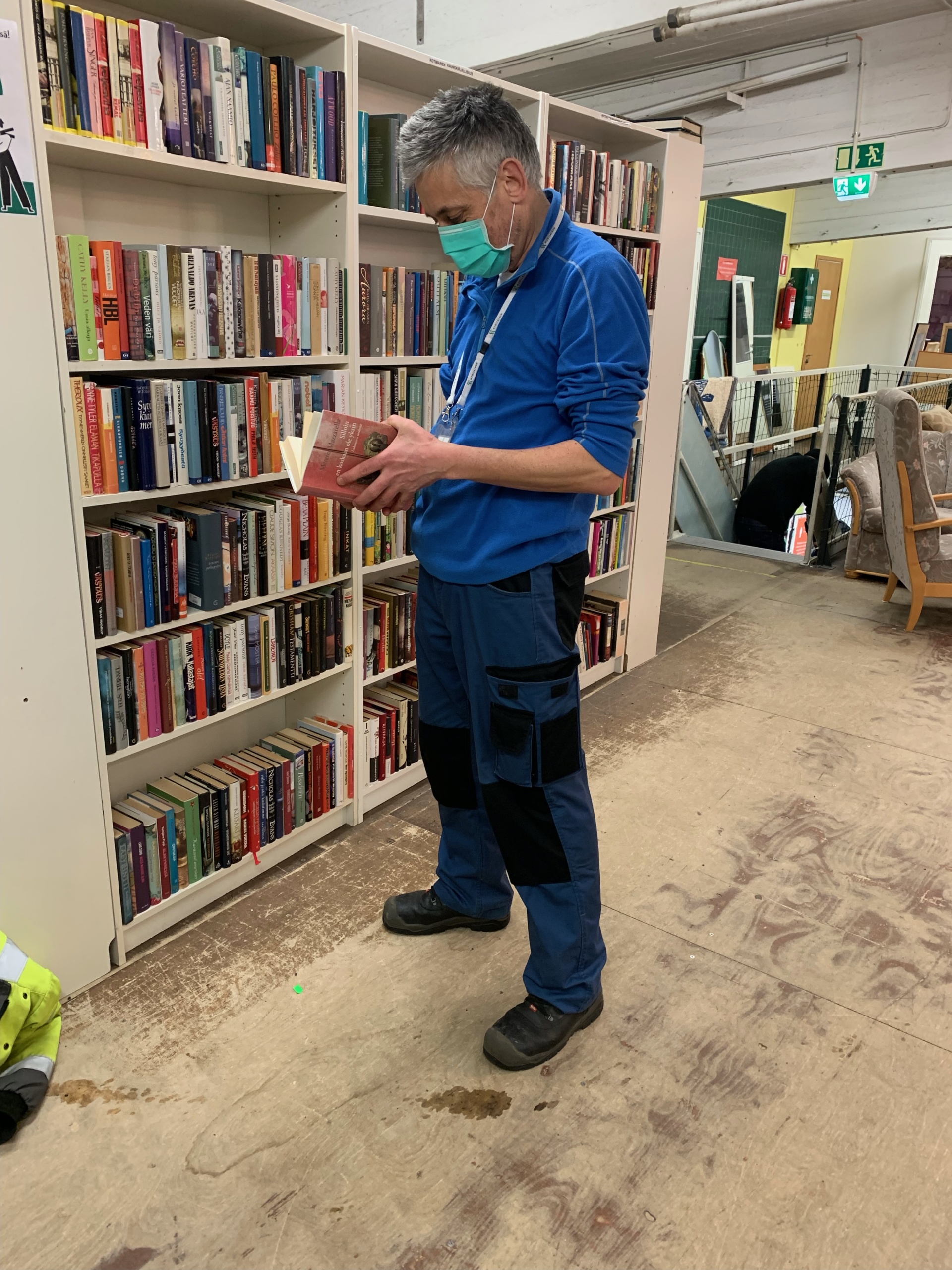Mies tutkii maski päässä kirjaa kirjahyllyn edessä.