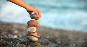 Käsi asettelee rannalla kiviä pinoon.