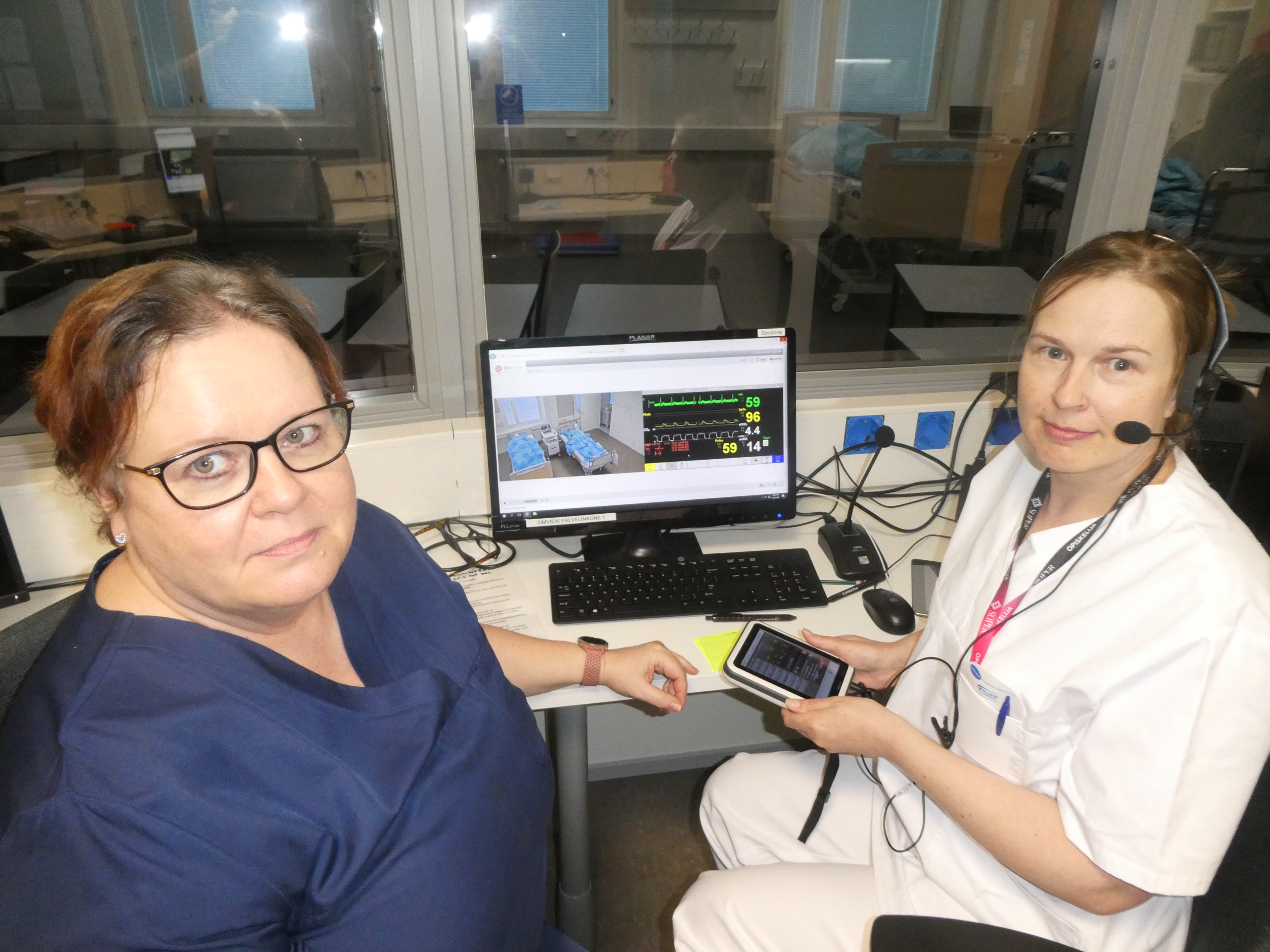 Kaksi hoitoasuihin puheutunutta naista istuu näyttöruudun äärellä valmomassa simulaatiohoitotilannetta.