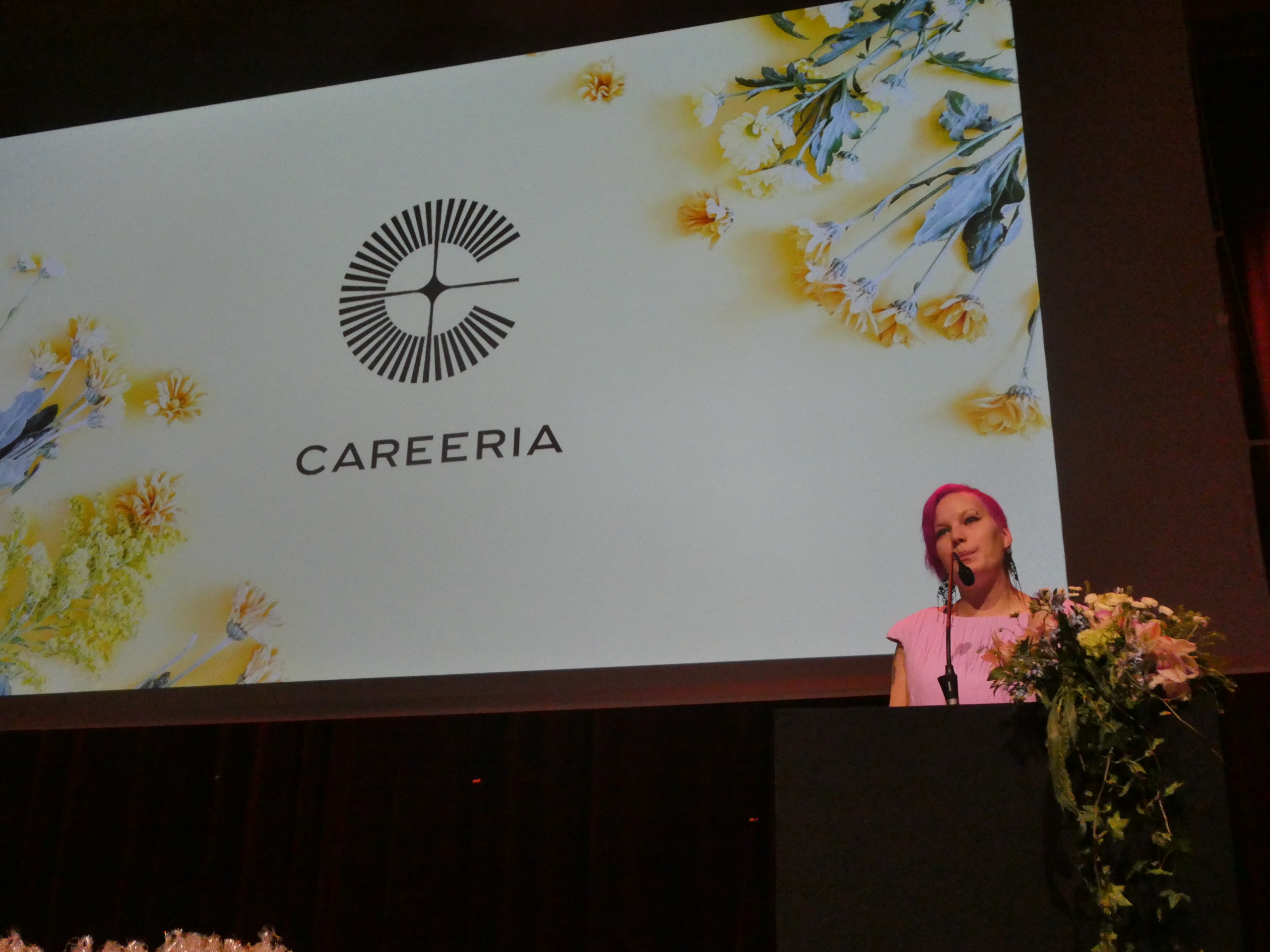 Nainen puhee mikrofoniin puhujanpöntössä, taustalla Careerian logo.
