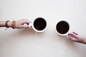 Kaksi kahvikuppia, joita pitää kaksi eri kättä.