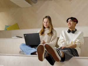Nuori nainen ja mies istuvat penkillä, tytöllä sylissä kannettava tietokone.