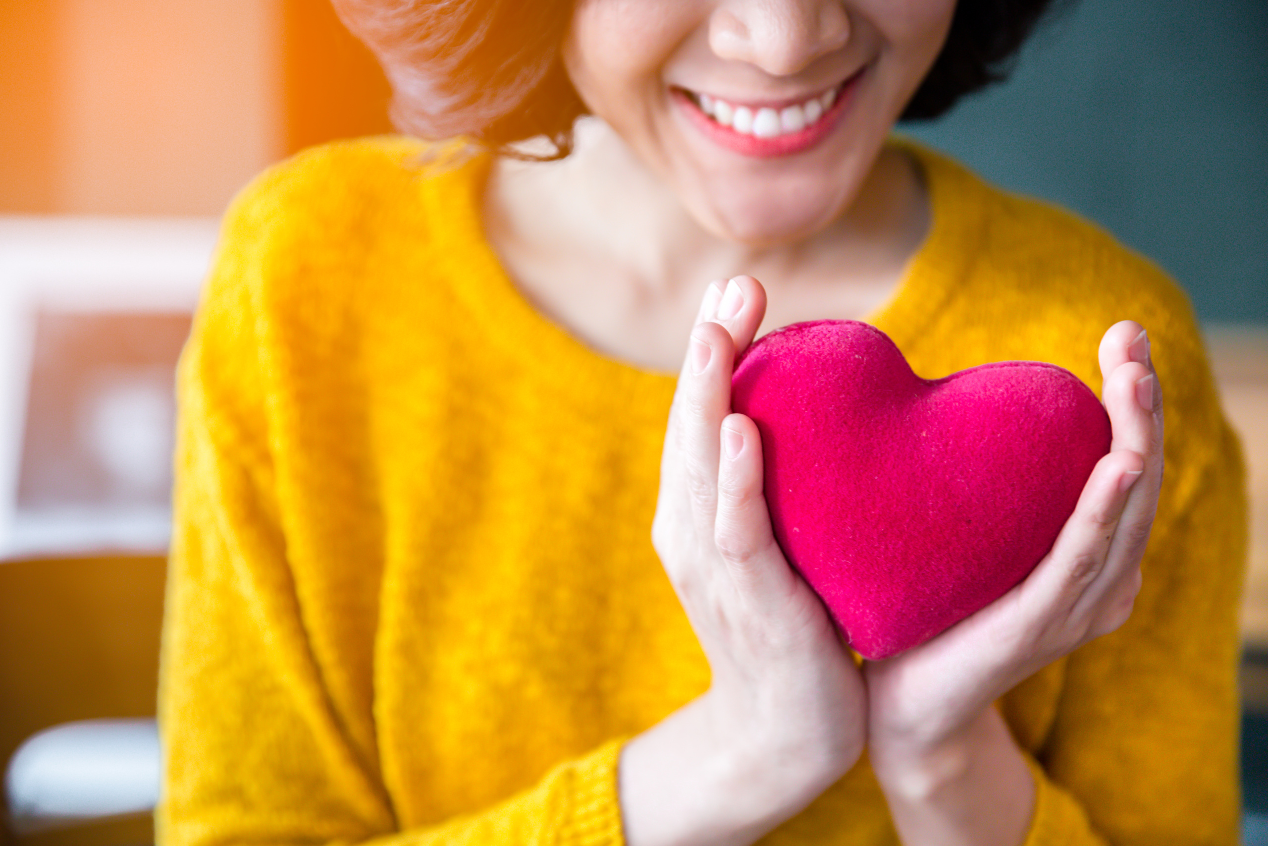 Hymyilevä keltapuseroinen nainen pitää käsissään punaista sydäntä.