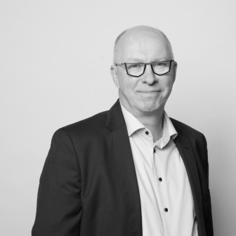 Silmälasipäinen mies pikkutakki yllään mustavalkoisessa profiilikuvassa.