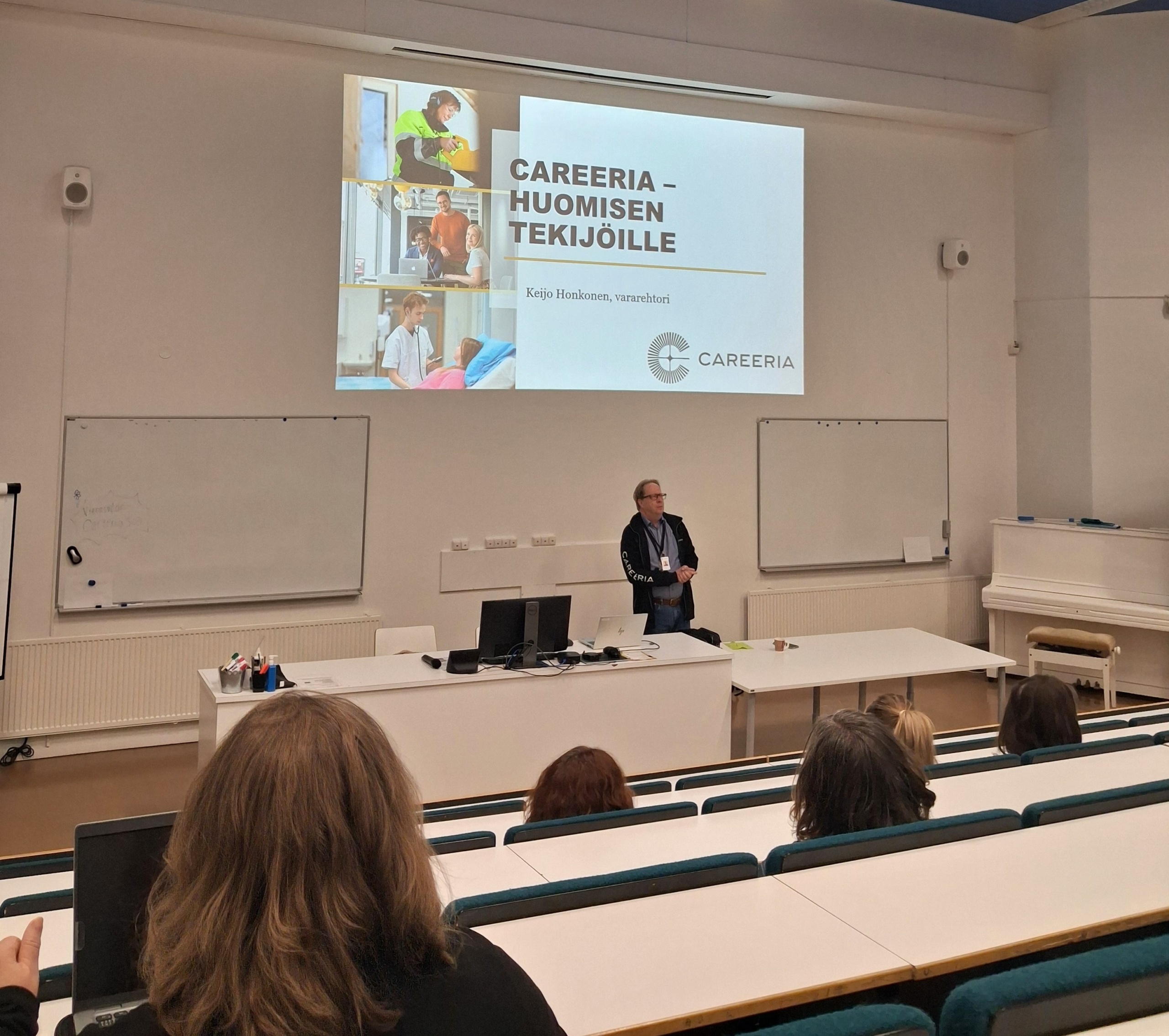 Mies pitämässä puhetta auditorion edessä. Taustalla kuva, jossa lukee Careeria - Huomisen tekijöille.
