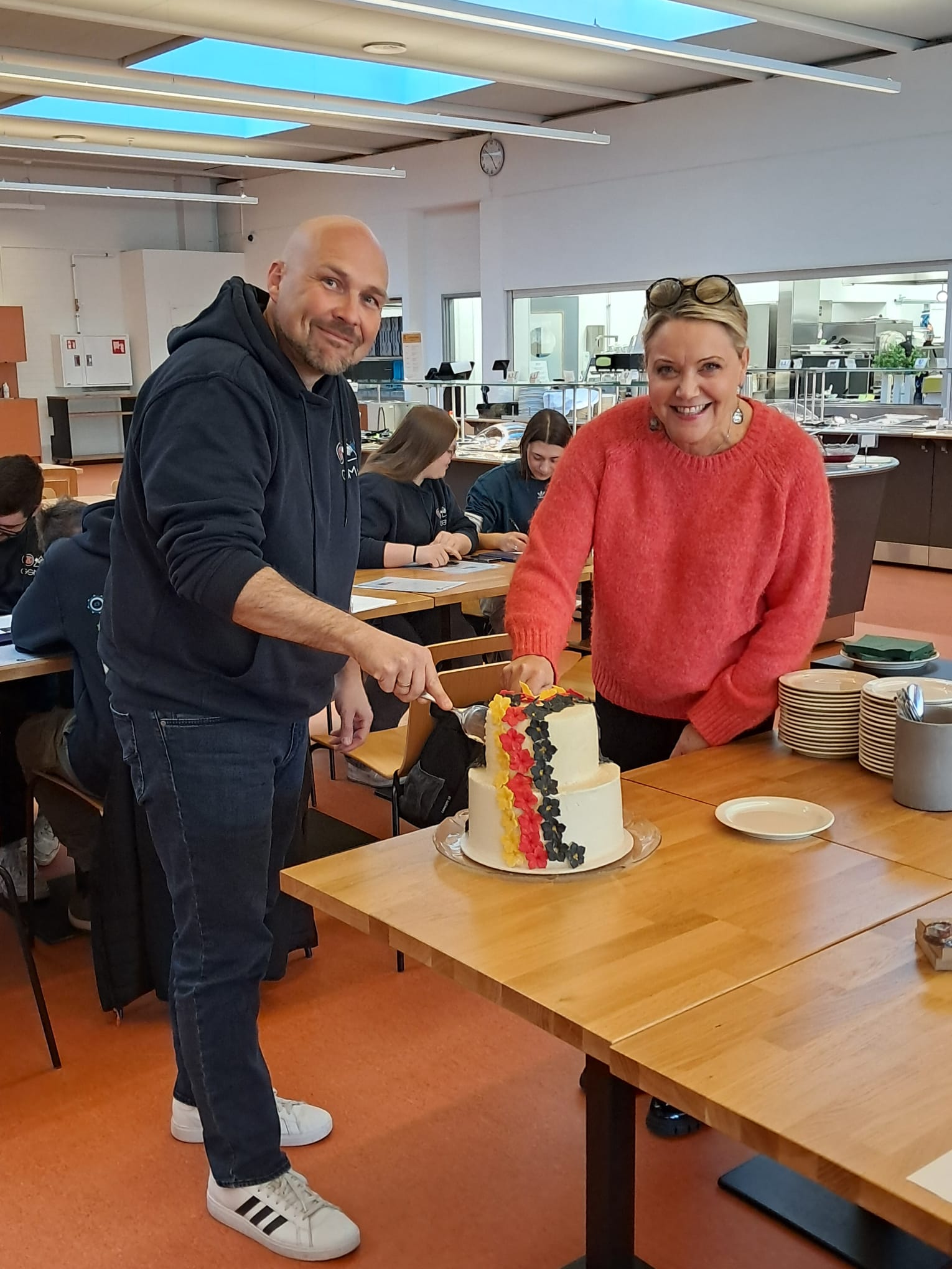 Hymyilevät mies ja nainen leikkaamassa kaksikerroksista kukkasin koristeltua kakkua.
