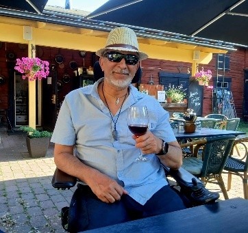 Aurinkolasipäinen mies päässään kesähattu ja kädessään juomalasi.
