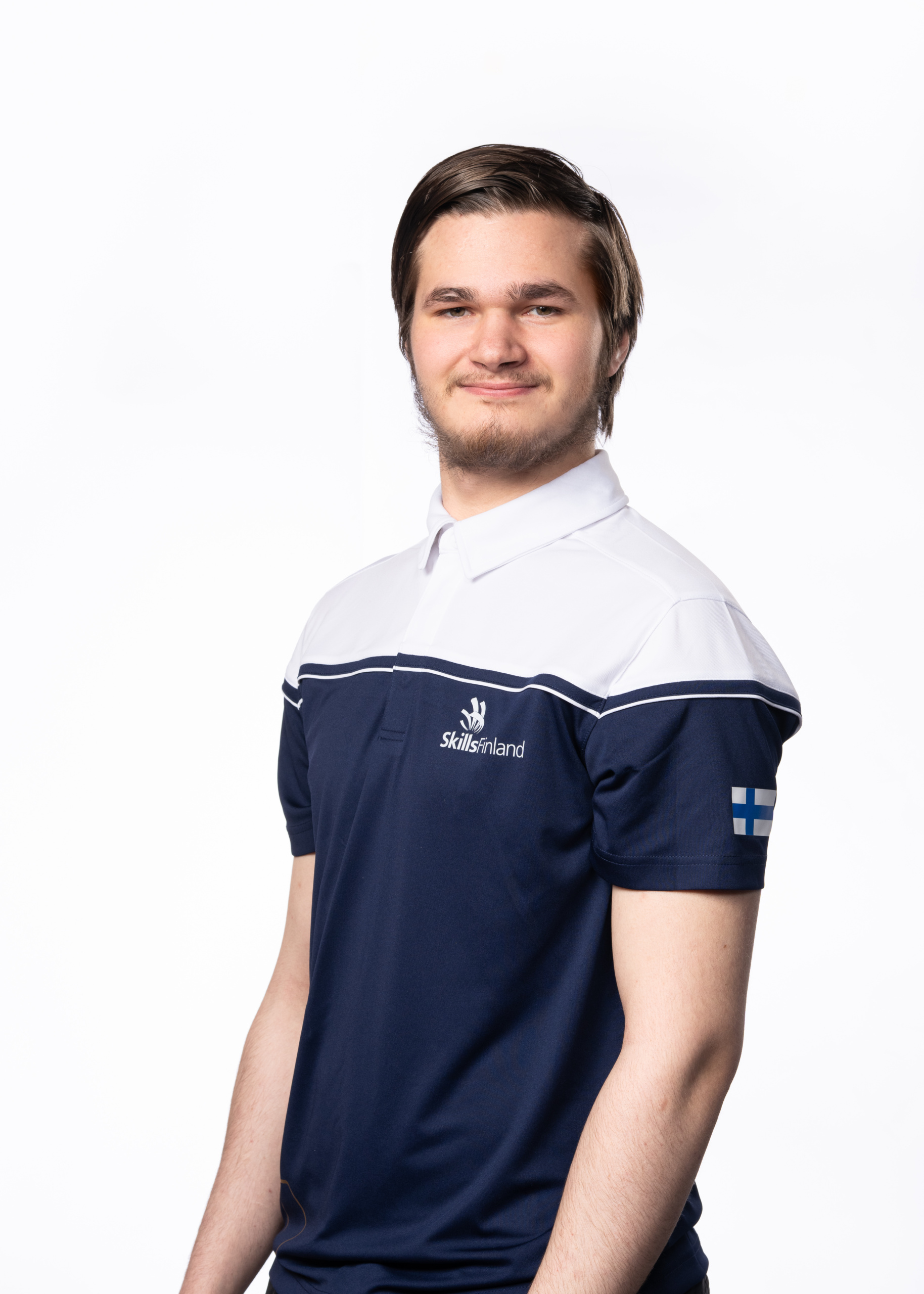 Nuori tummahiuksinen mies yllään Skills Finlandin Suomen maajoukkueen edustuspaita.