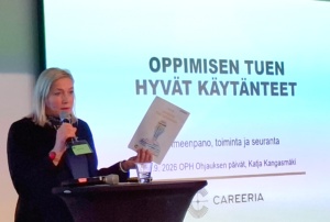 Nainen pitämässä luentoa. Taustalla näkyy otsikko: Oppimisen tuen hyvät käytänteet.
