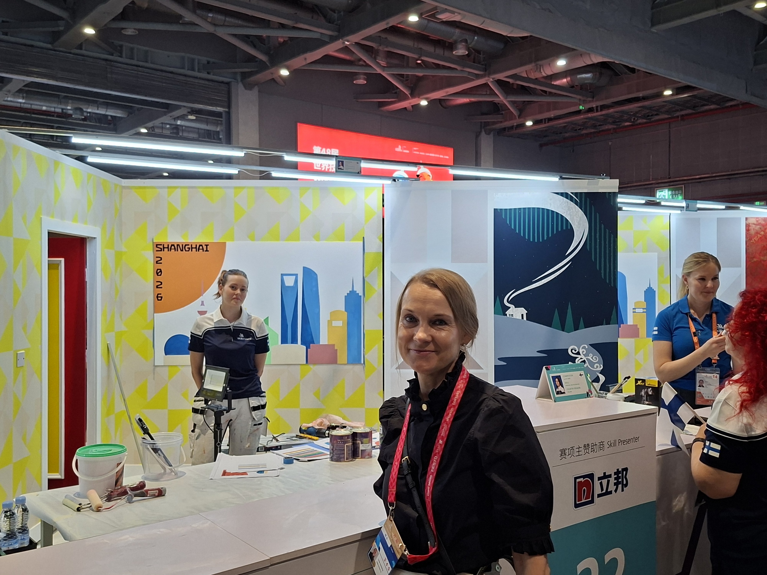 Careerian kilpailija kilpailutyönsä äärellä WorldSkills Shanghai 2026 -kilpailussa. Kuvassa myös kilpailijan opettaja ja viereisessä tilassa kilpaileva henkilö ohjaajansa kanssa.